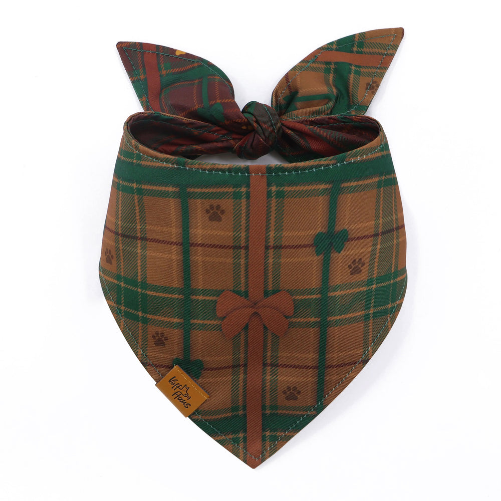 The Bark The Halls reversible dog bandana tied and laid flat, showing the chestnut plaid side with a bow and paw prints